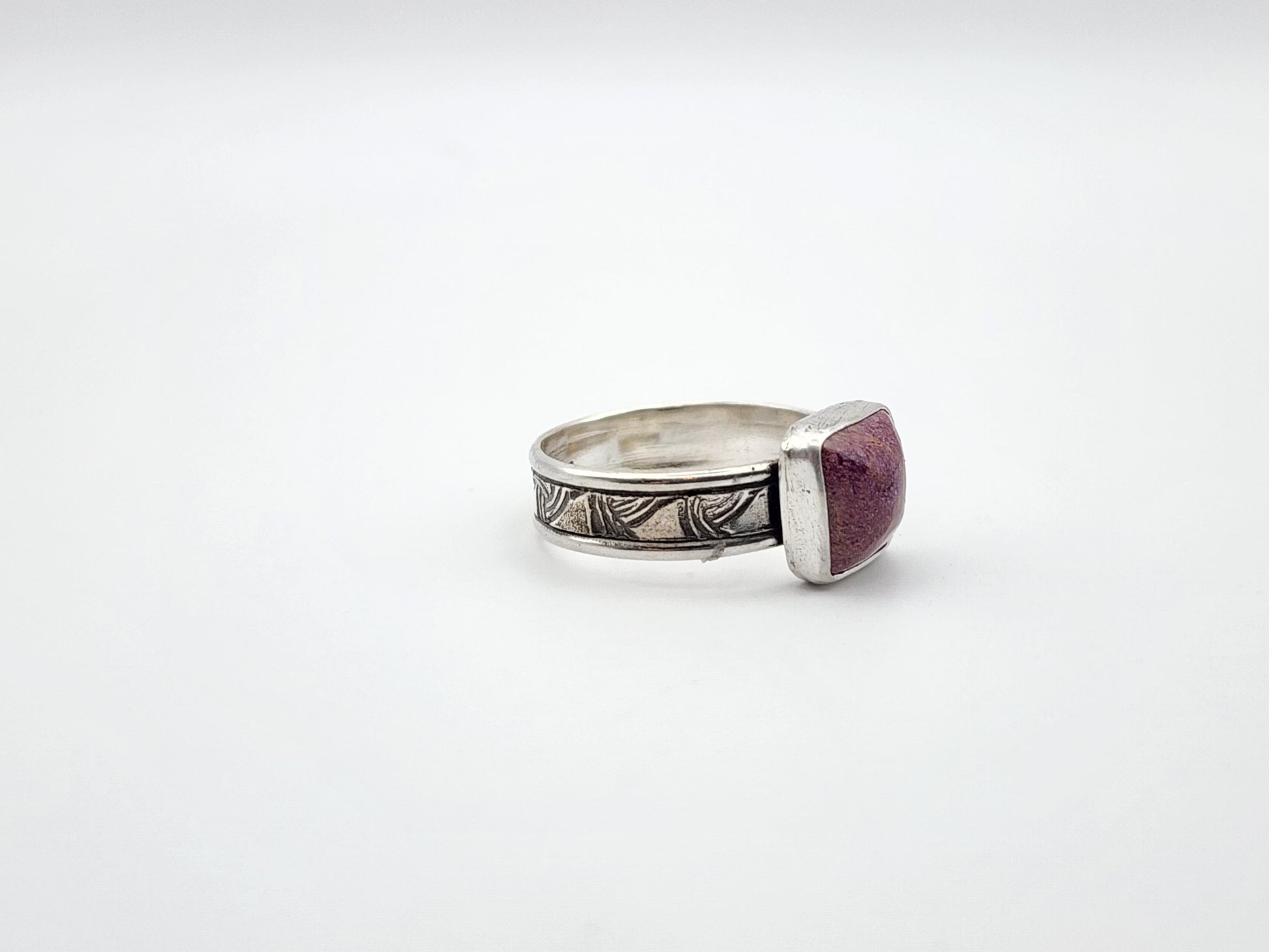 Silver ring with a stichtite gemstone on a white background. side view of ring