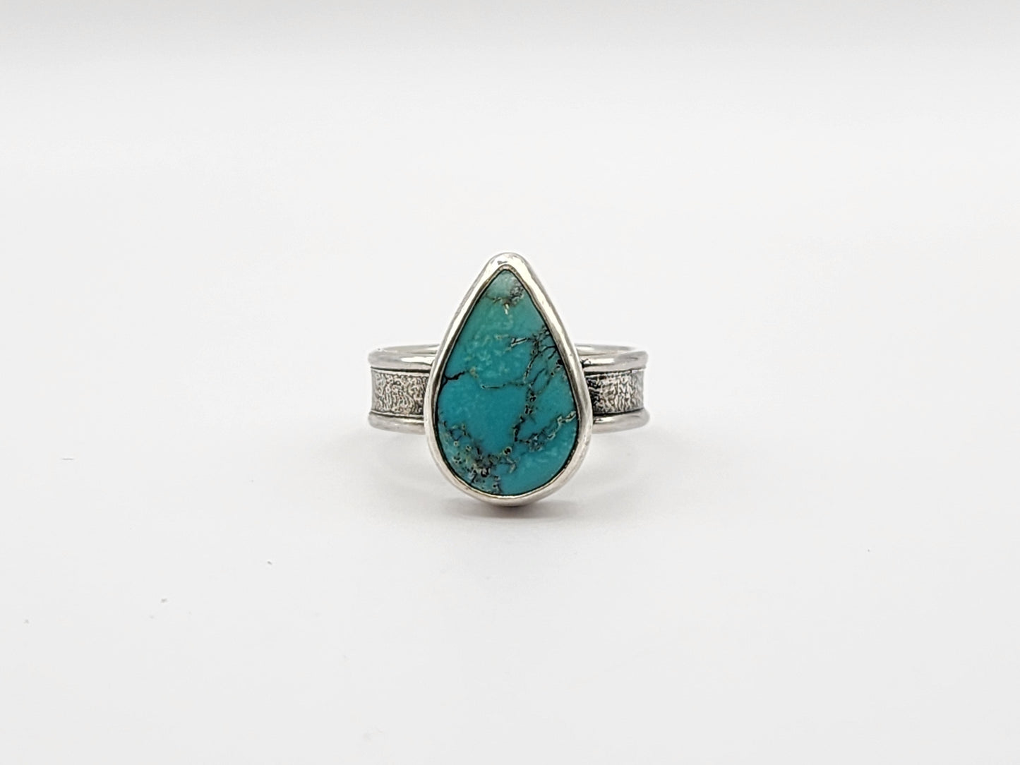 Front view of turquoise ring with textured silver band on a white background