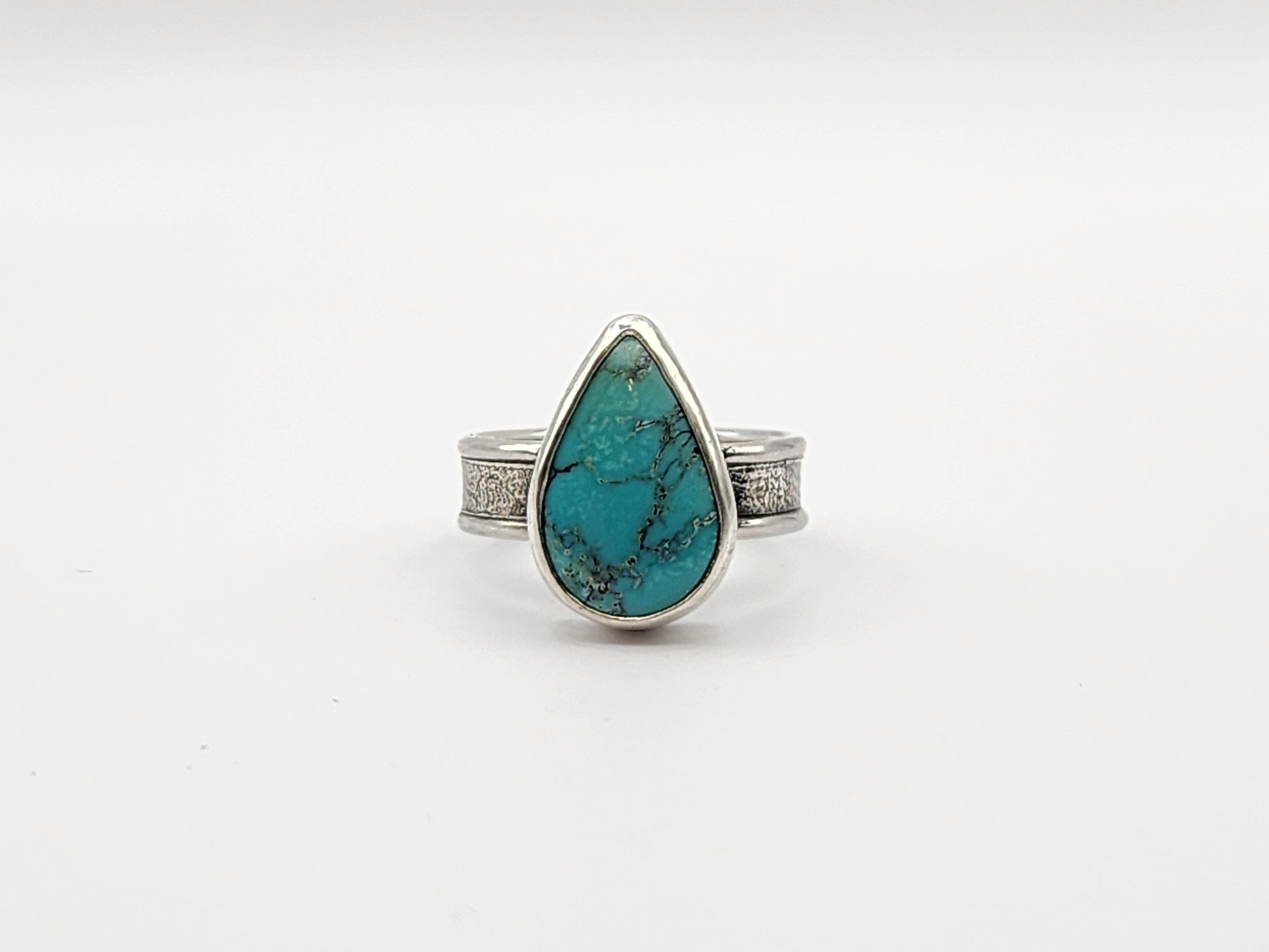 Front view of turquoise ring with textured silver band on a white background