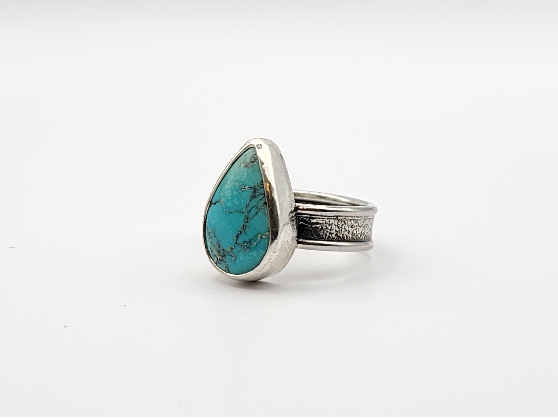 Side view of silver ring with a teardrop shaped turquoise stone on a white background. 
