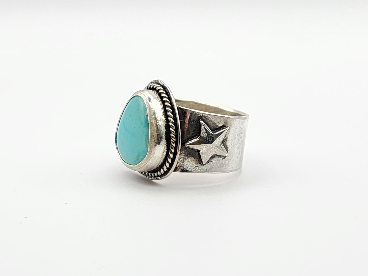 Side view of silver ring with turquoise stone and star design on a white background