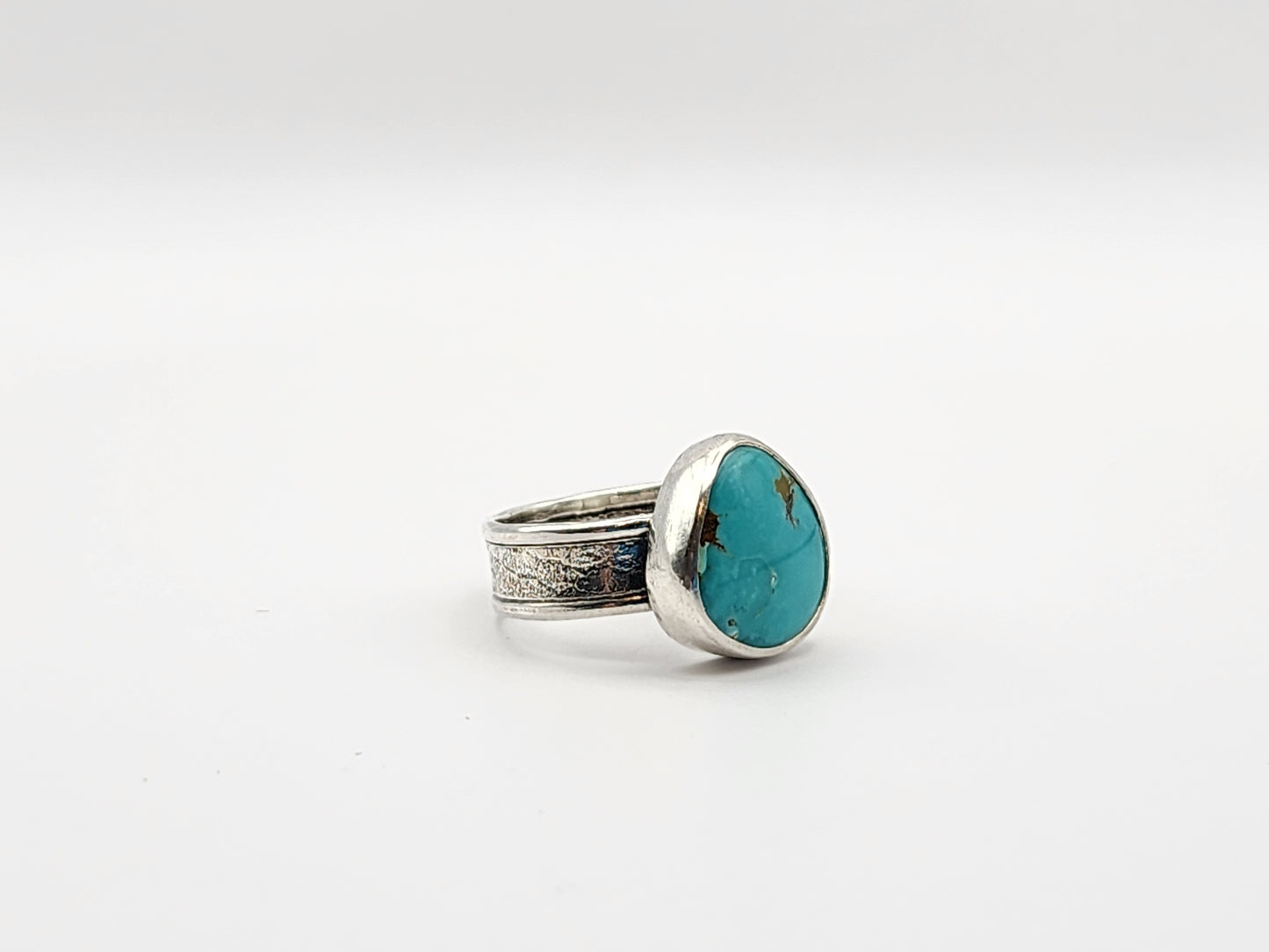 Side view of silver ring with a turquoise stone on a white background