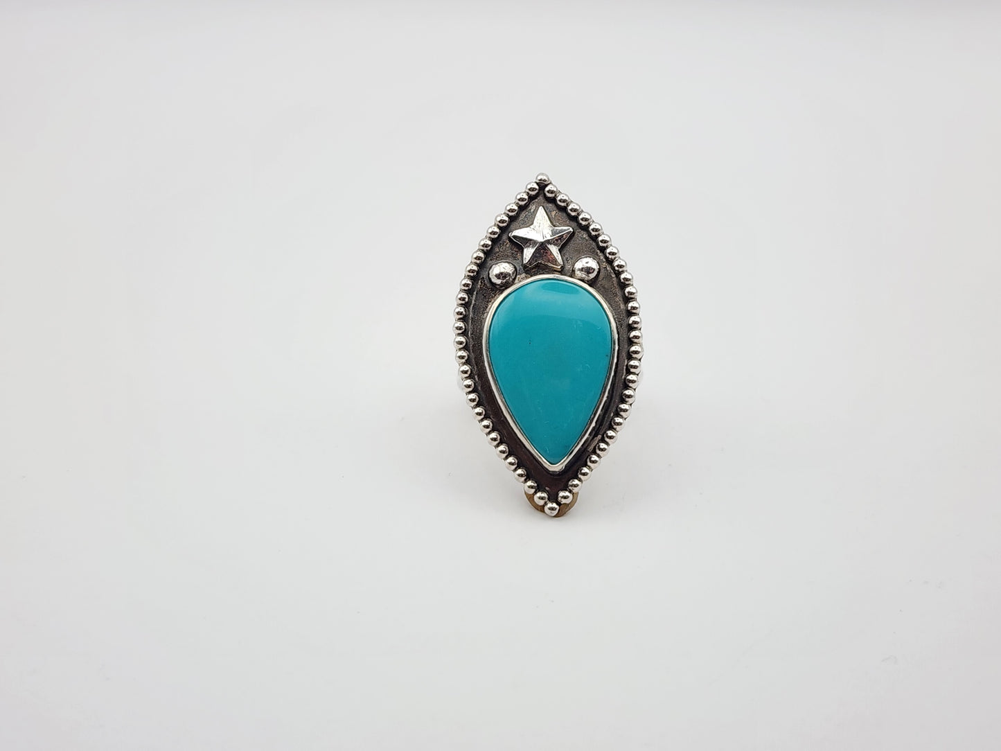 Front view of turquoise stone ring with star, silver balls and border with silver band on a white background