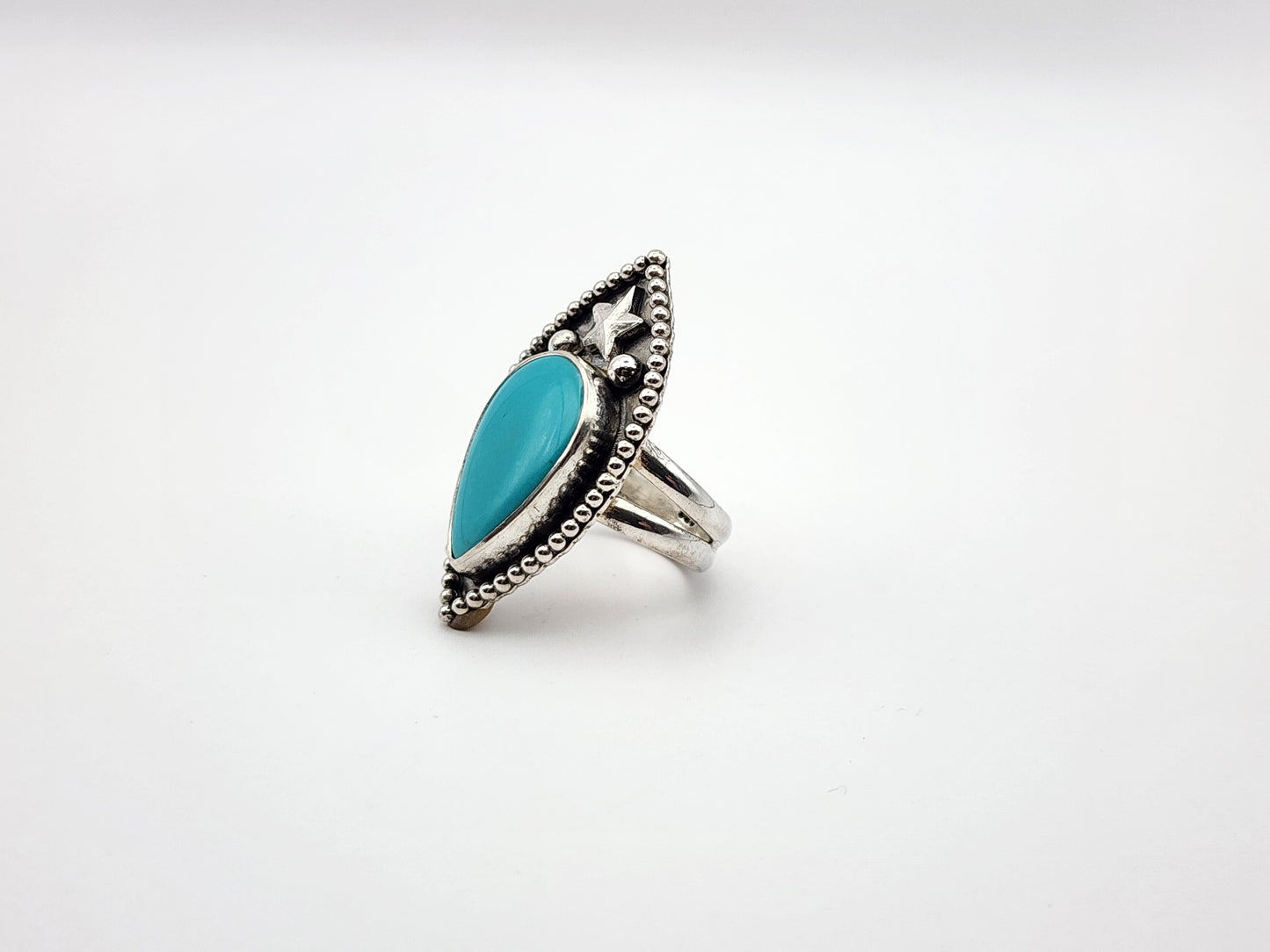 Side view of silver ring with a turquoise stone with star and two silver balls and border on a white background
