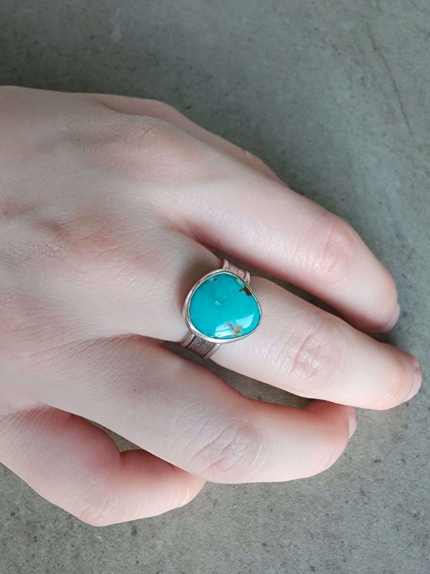 Hand wearing a turquoise ring on a neutral background