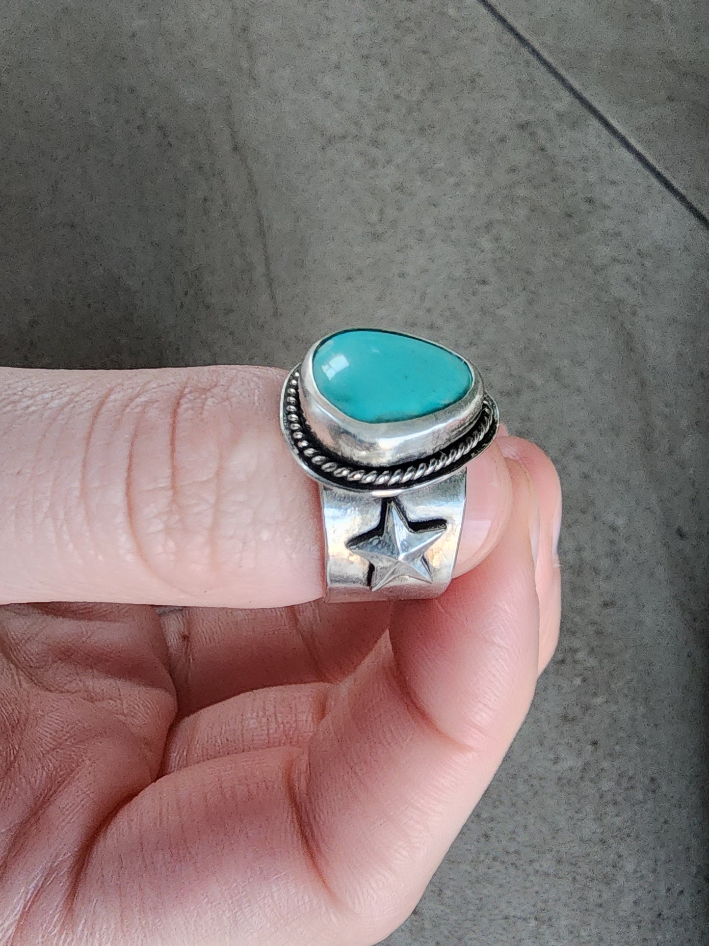 Silver ring with a turquoise stone held on a neutral background