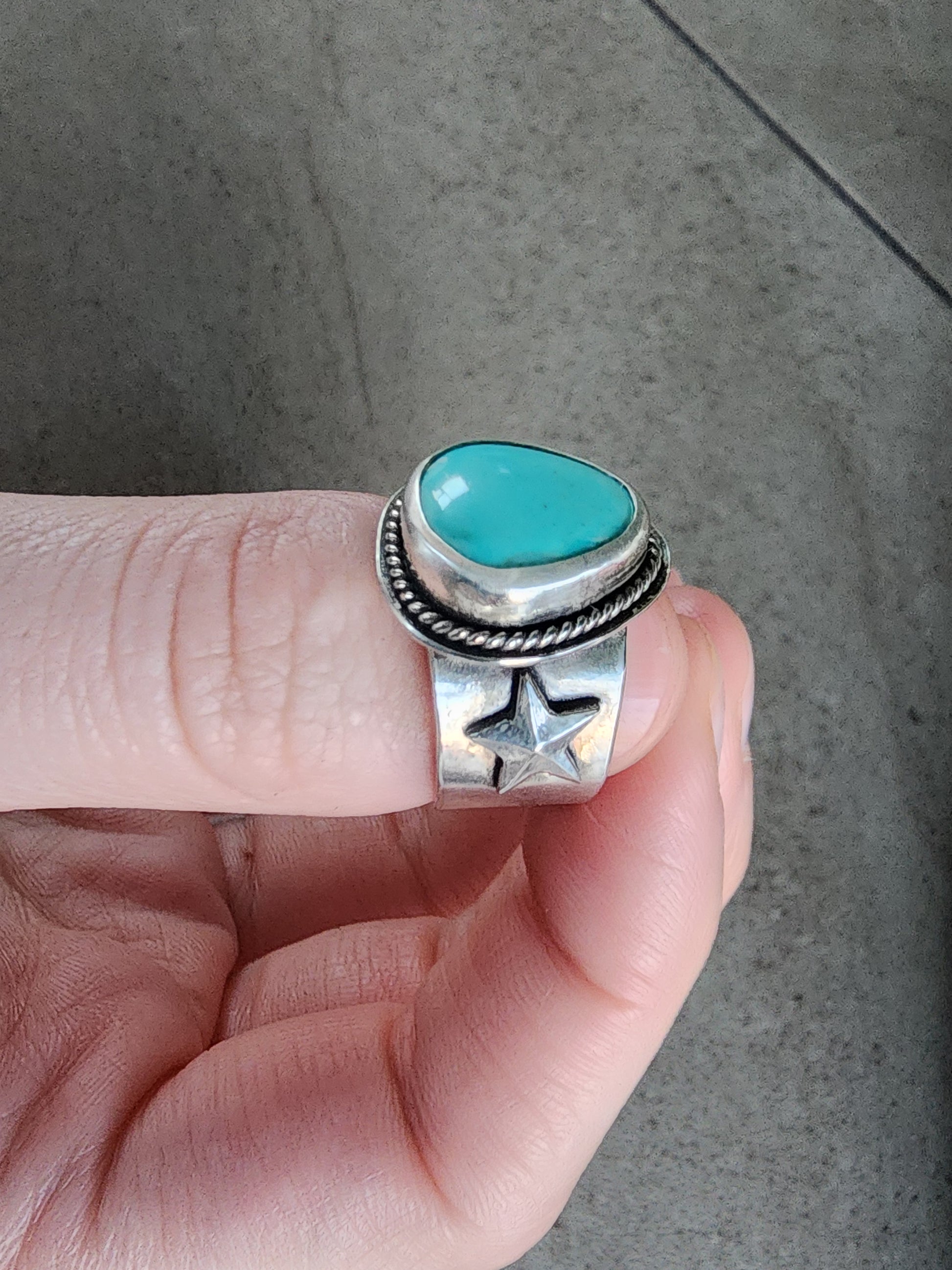 Silver ring with a turquoise stone held on a neutral background