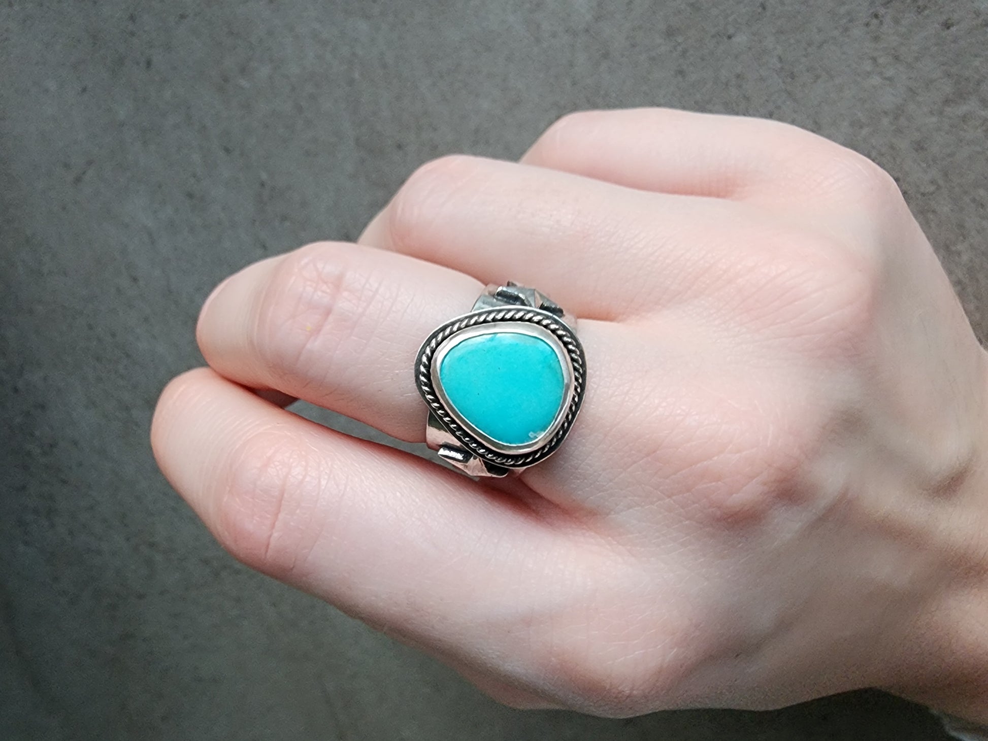 Hand wearing a turquoise stone ring with silver band on a neutral background