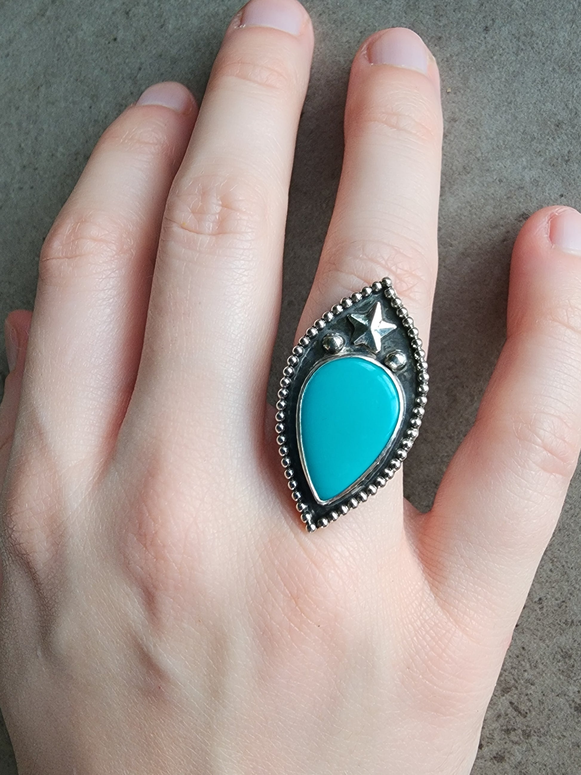 Turquoise ring with star, two silver balls and border with silver band on a hand against a neutral background