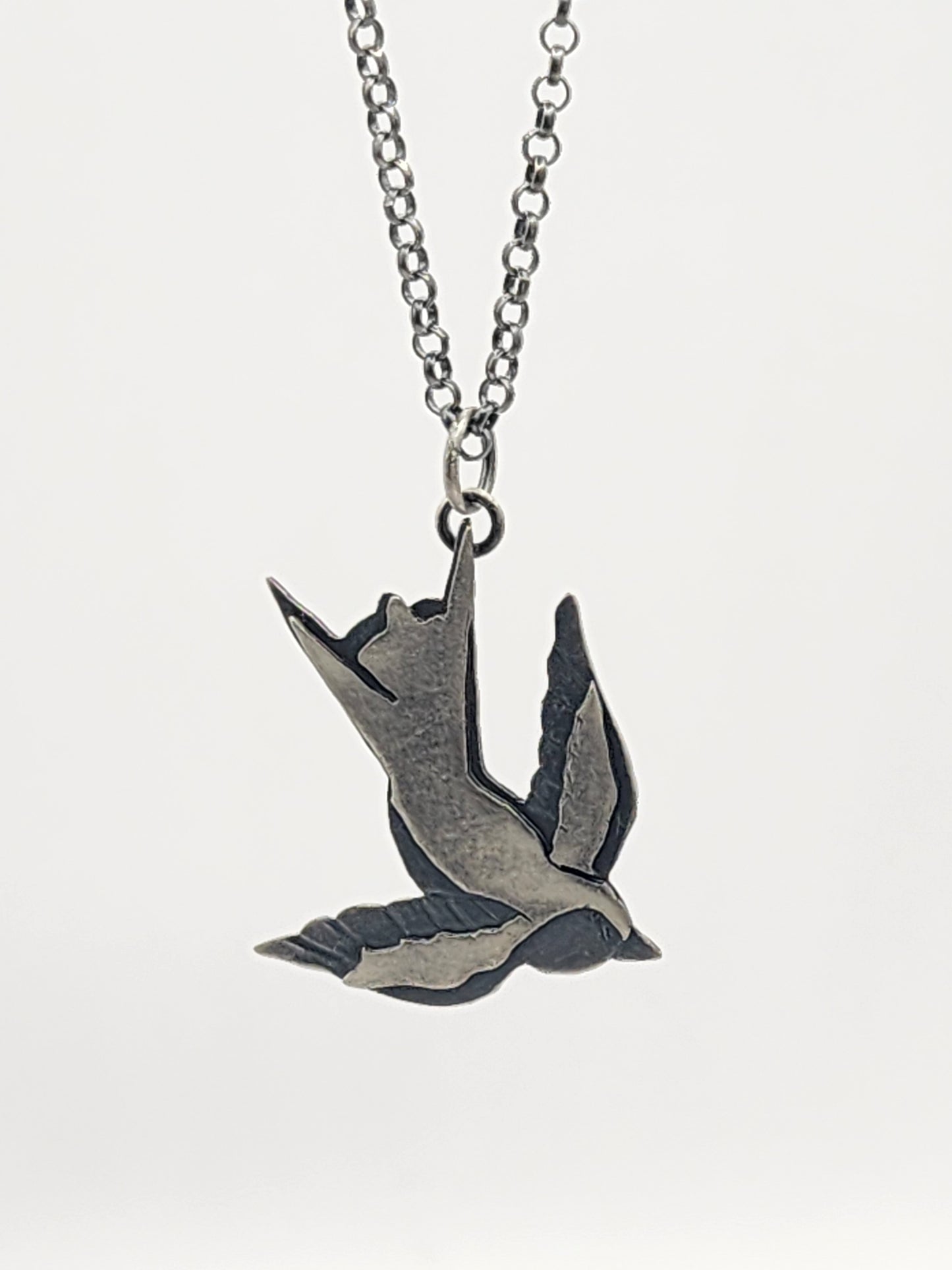 A silver-toned metal pendant necklace featuring a flying bird design, suspended from a matching chain against a white background.
